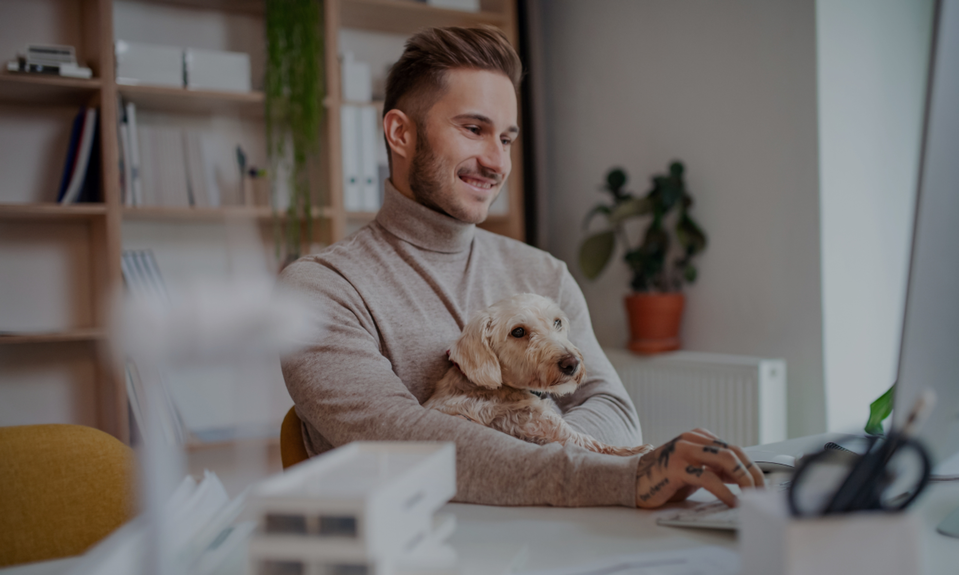 Young businessman with dog sitting at the desk indoors in office, using computer.