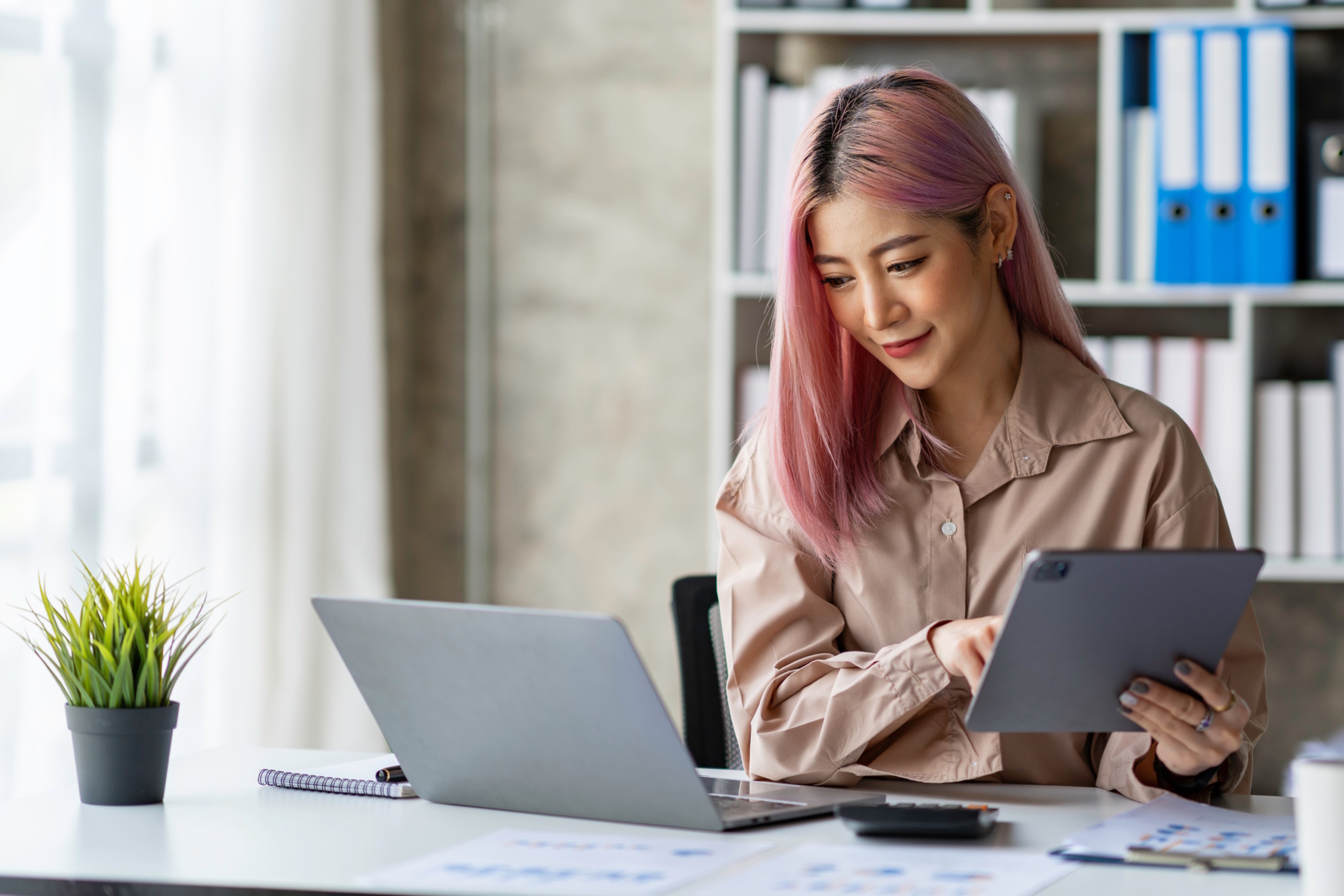 Portrait of a young Asian businesswoman working on a tablet with a laptop at the thinking office. analyze marketing data online business ideas.