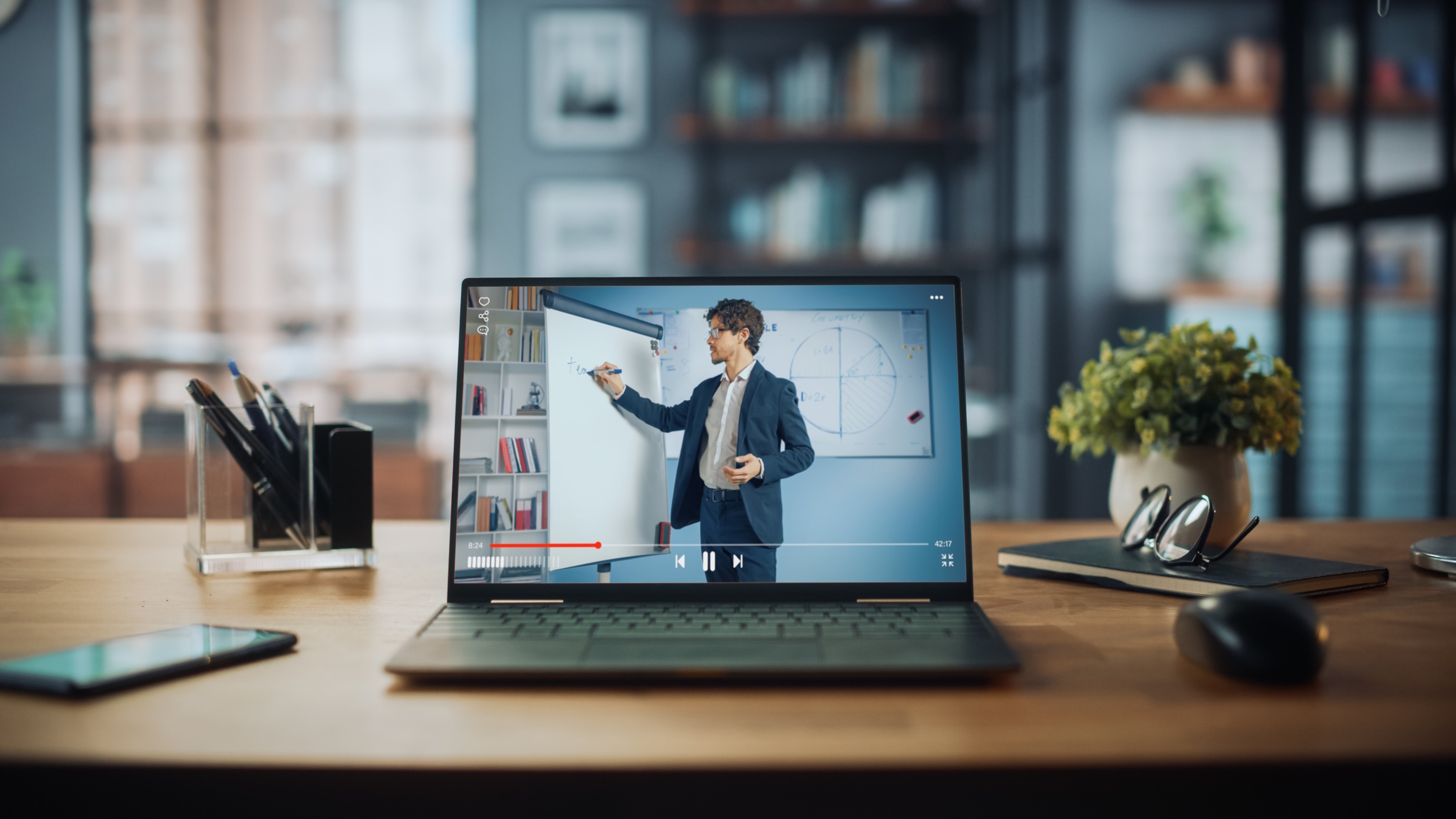 Shot of a Laptop Computer Showing Online Lecture with Portrait of a Cute Male Teacher Explaining Math Formulas. It is Standing on the Wooden Desk in Stylish Modern Home Office Studio During Day.